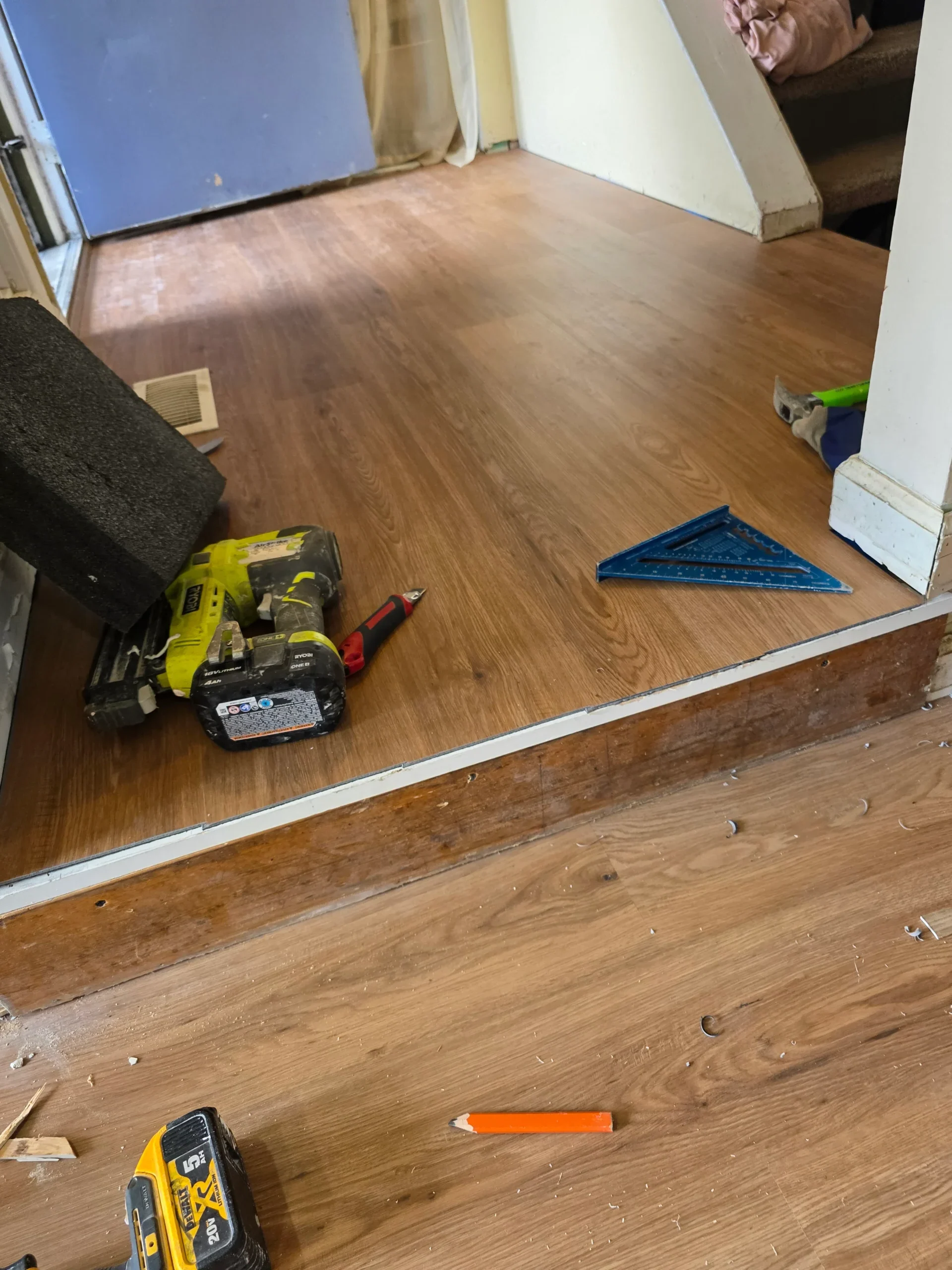 Plank flooring being fitted through a doorway with tools on the floor