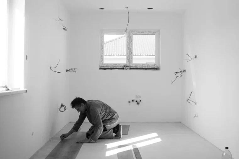 Installer installing laminate flooring planks row by row in an empty room