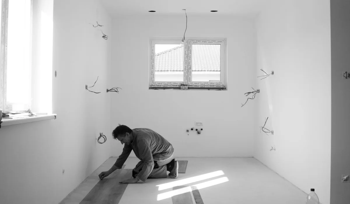 Installer installing laminate flooring planks row by row in an empty room