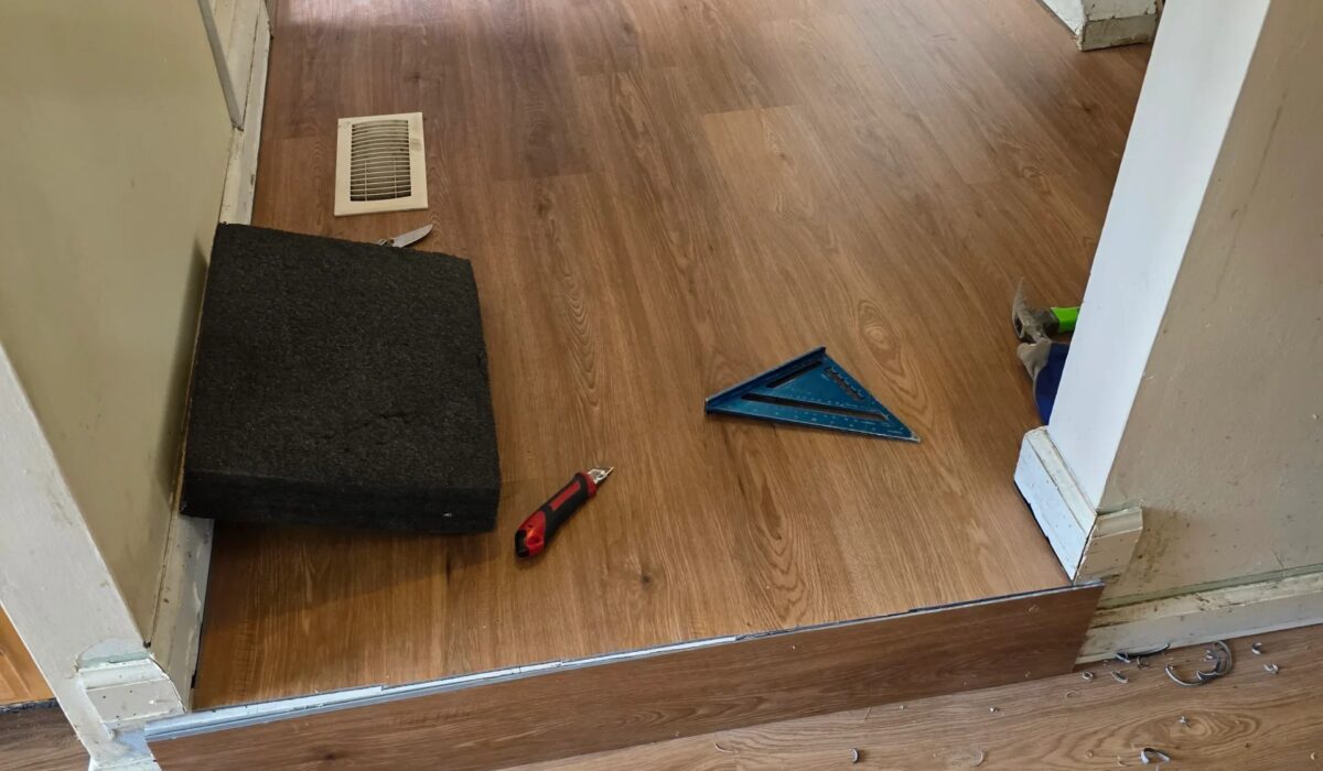 Laminate planks cut to a step edge with a speed square, where a laminate flooring calculator adds extra waste