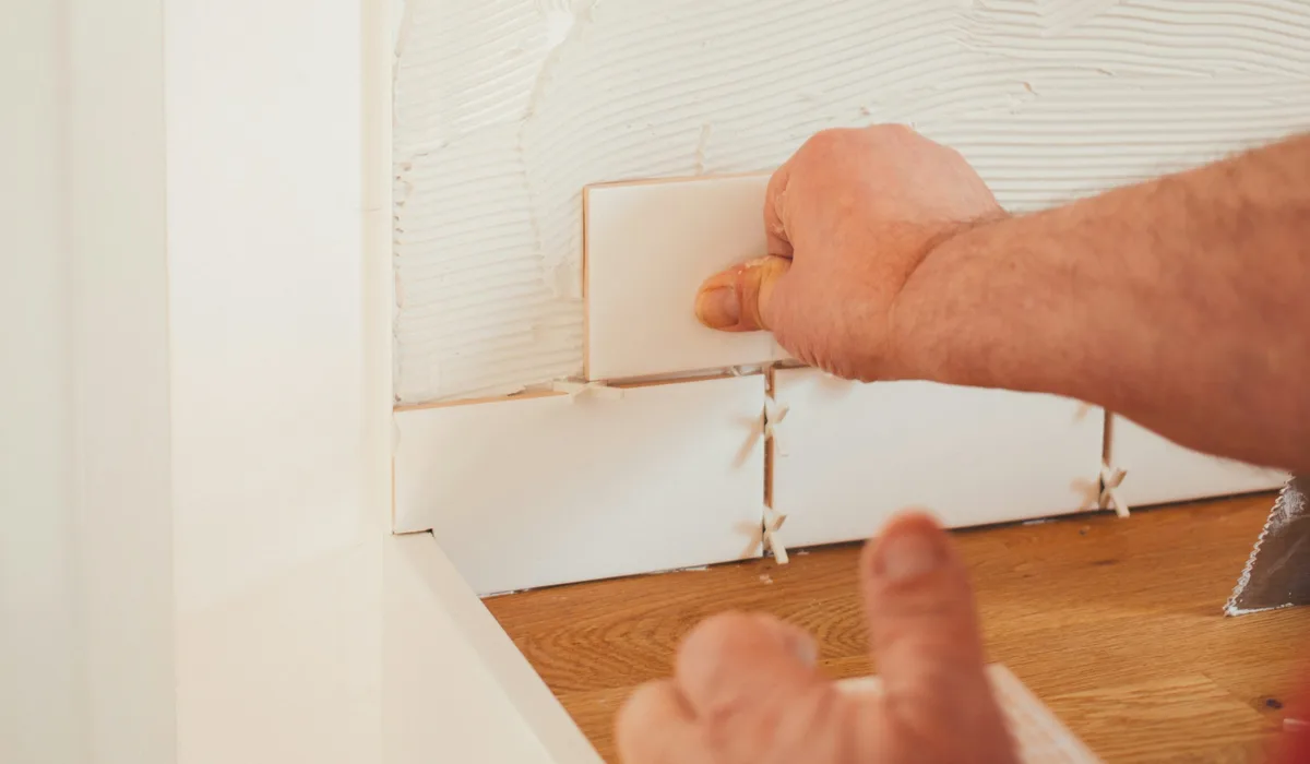 Installer pressing a white tile into place with spacers to keep the grout joints even