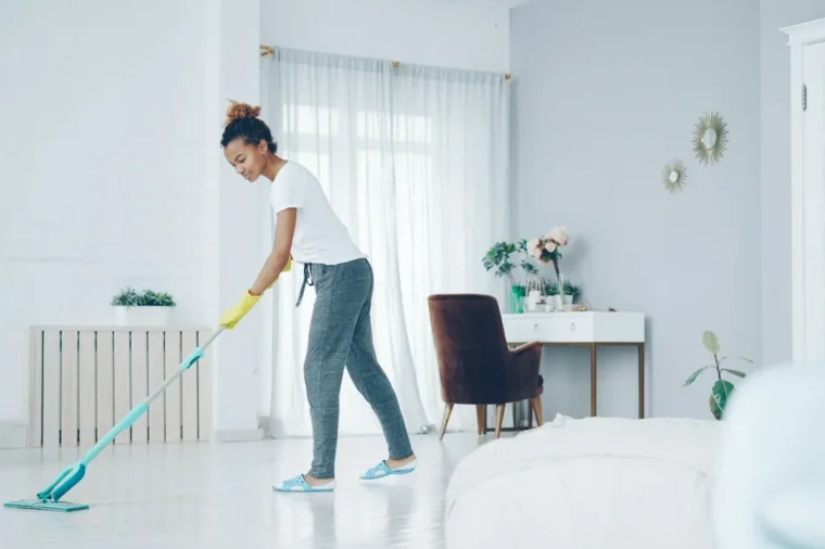 Damp mopping a vinyl plank floor in a bright living room with a microfiber mop
