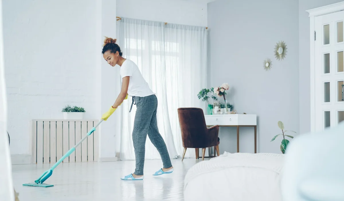 Damp mopping a vinyl plank floor in a bright living room with a microfiber mop